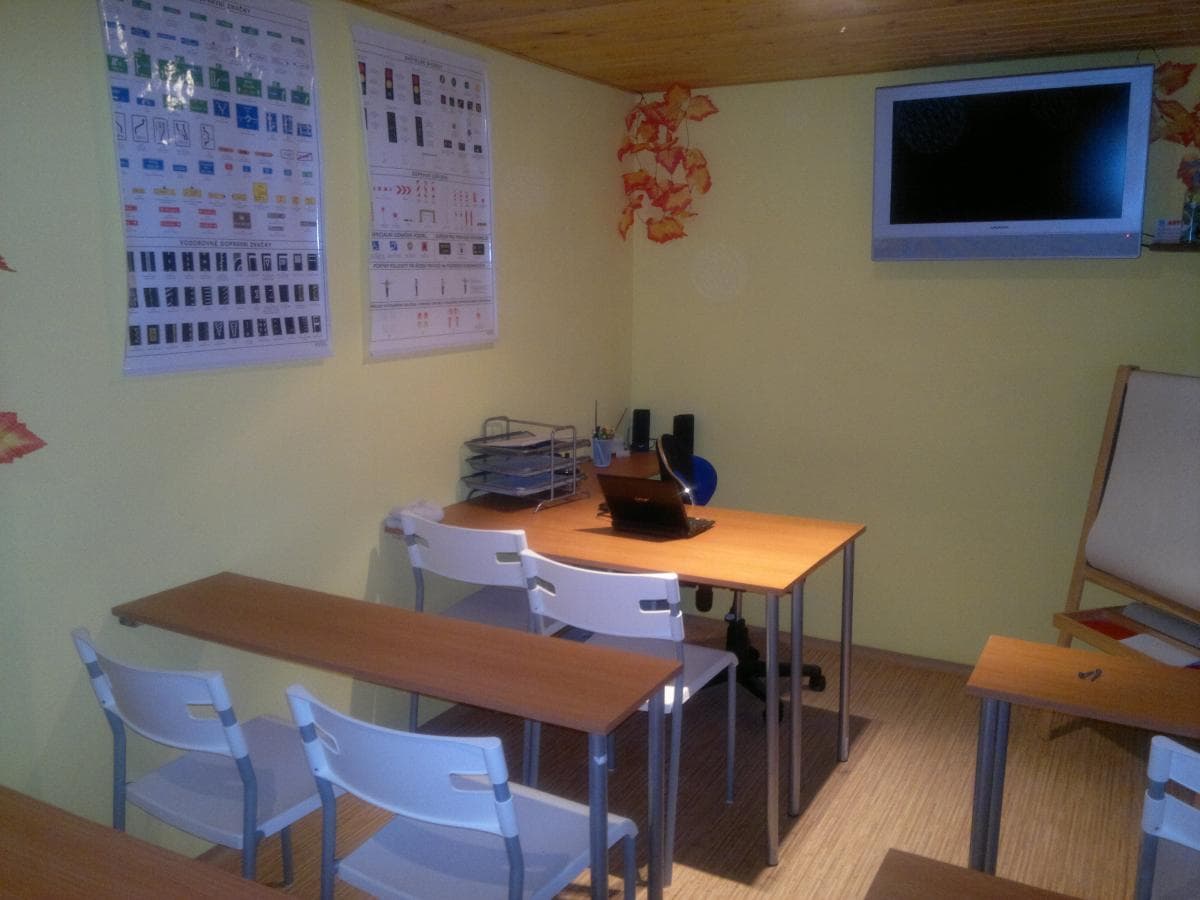 Učebna autoškoly: lavice se židlemi, na stěně tabule dopravních značek a televize