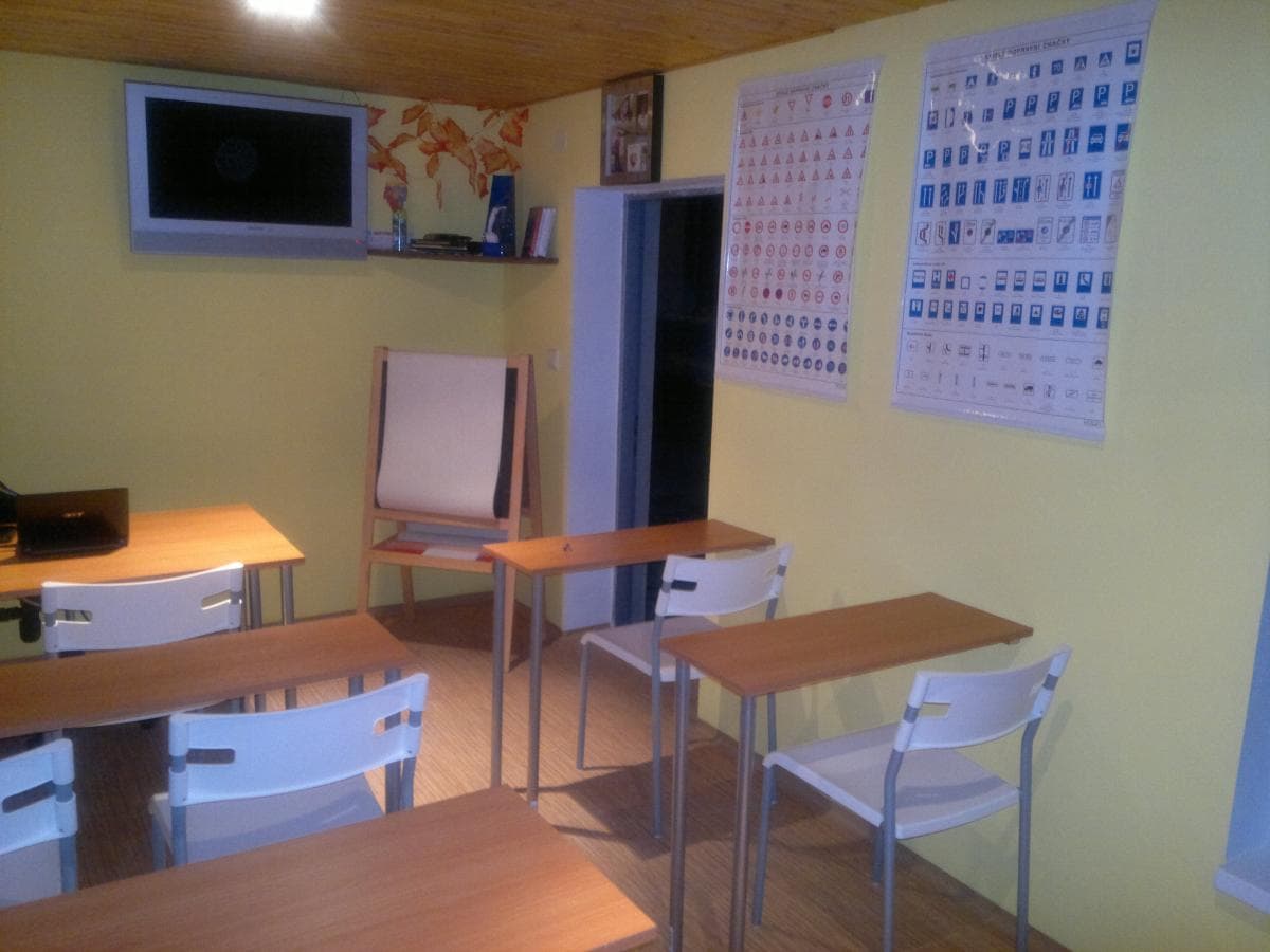 Druhý pohled do učebny s lavicemi, flipchartem a přehledem značek na stěně